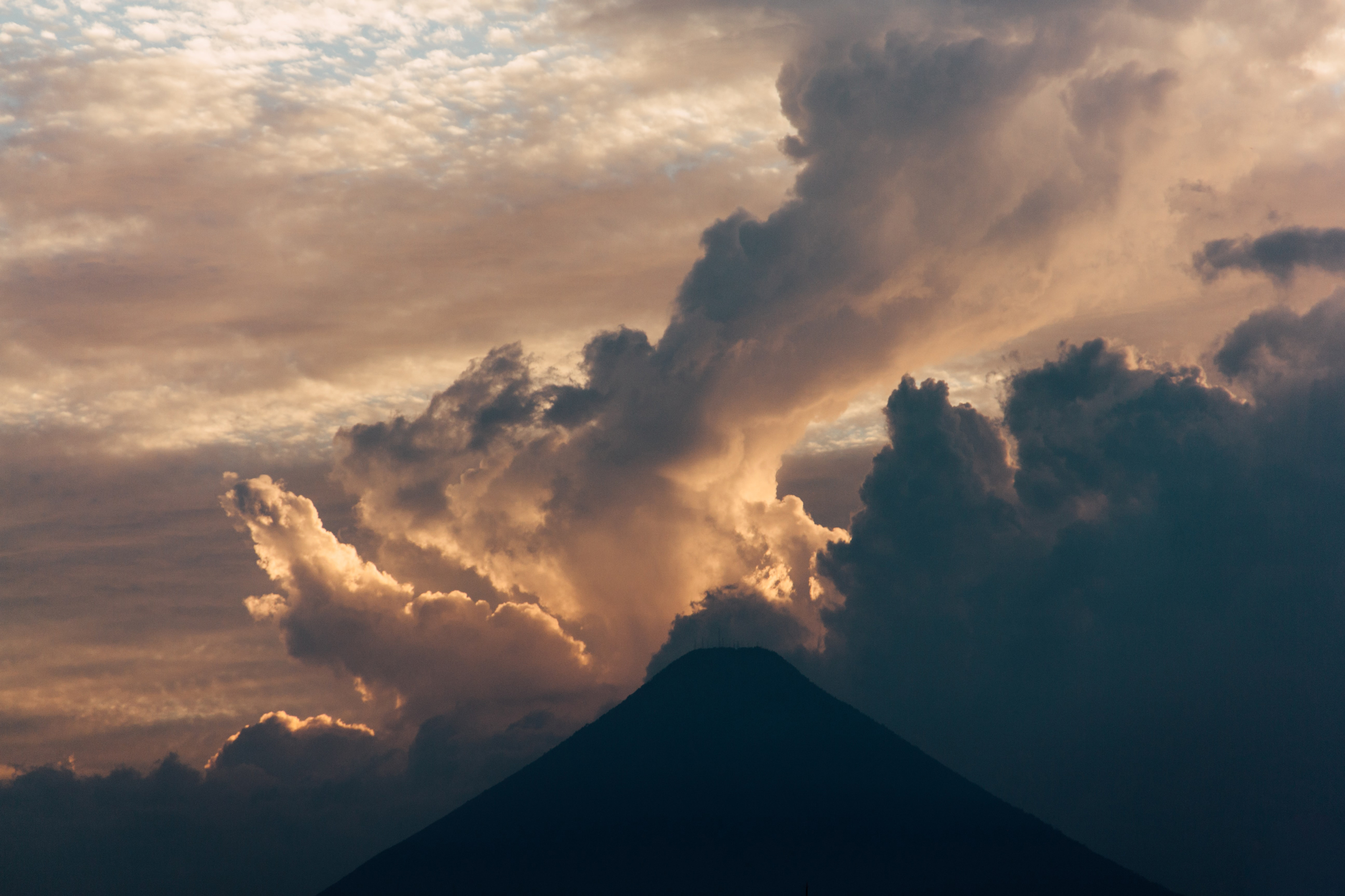 A volcano with clouds rising over.